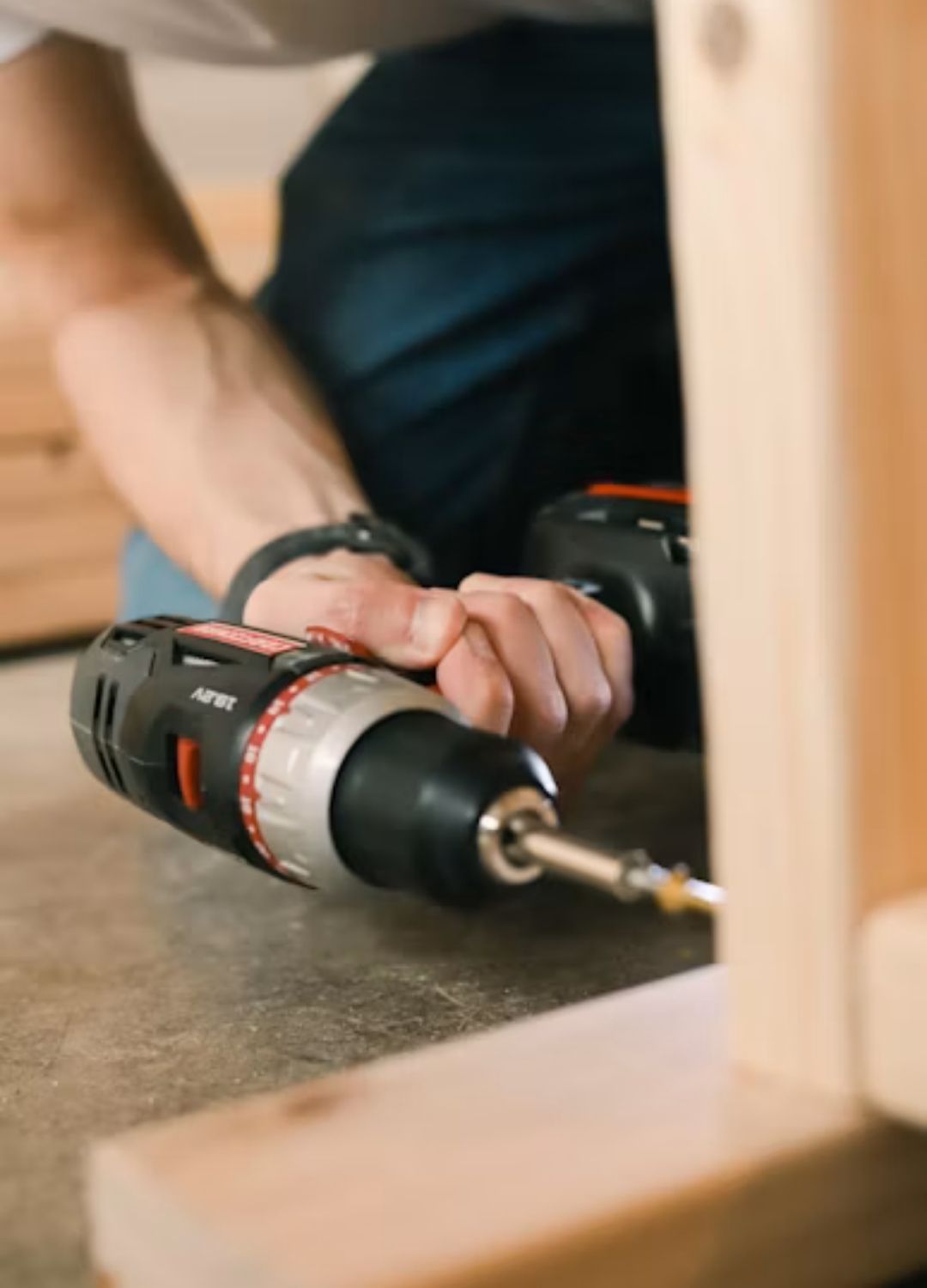 Close-up of a drill securing a metal folding bracket onto a plywood desk leg with wood screws.