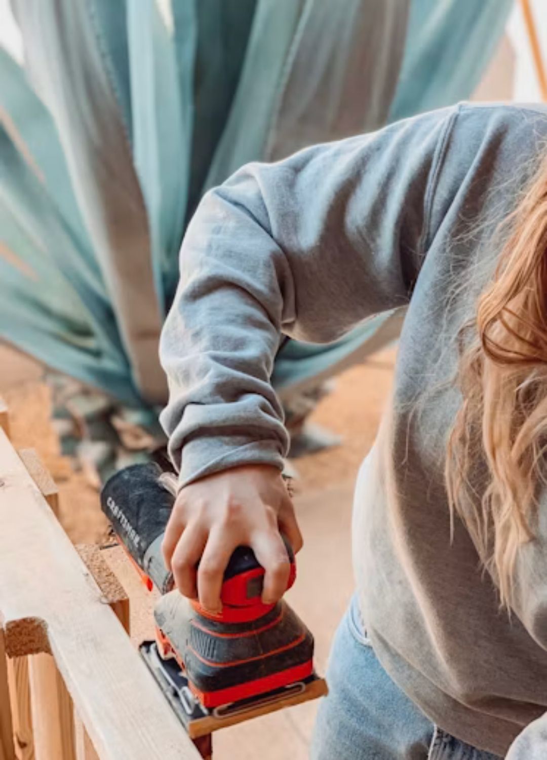 Sanding the edges and surface of a plywood study desk with an orbital sander for a smooth finish.